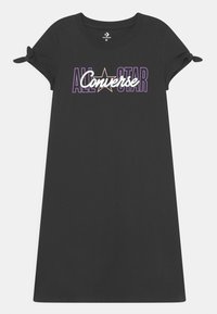 Czarna bawełniana sukienka typu t-shirt z krótkimi rękawami, z węzłowymi detalami oraz grafiką "ALL STAR Converse" w purpurowym i białym napisie.