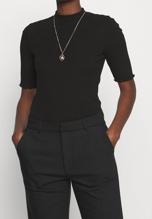 Haut noir à manches courtes côtelé avec un col montant et des manches à volants, associé à un pantalon noir ajusté. Un collier doré ajoute une touche de détail.