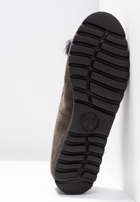 Zapato de ante marrón con una suela de goma negra texturizada, que cuenta con profundas ranuras para tracción y acentos decorativos en el lateral.