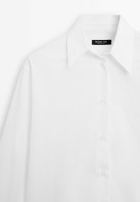 Chemise blanche à manches longues boutonnée avec un col pointu et une étiquette Massimo Dutti à l'intérieur de l'encolure.
