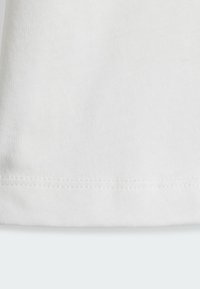 Tissu en coton blanc avec une surface lisse légèrement texturée. Présente un ourlet droit avec une couture visible le long du bord.