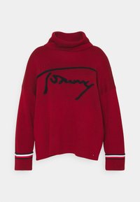 Czerwony sweter z dzianiny z wysokim kołnierzem, z czarnym haftowanym logo na klatce piersiowej oraz paskowymi akcentami na mankietach.