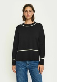 Pulover negru din tricot cu guler alb rotund și o dungi orizontale pe mijloc. Mâneci lungi și croială lejeră. Asortat cu blugi albaștri.