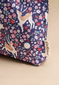 Tumšu zilu auduma soma ar rozā un baltu ziedu rakstu, kas ietver briežu un ziedu attēlus; iekļauts uzlīme ar "Cath Kidston" zīmolu.
