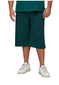 Donkergroene shorts met witte stippen, knielang, gemaakt van zachte stof. Gecombineerd met witte sneakers voor een casual uitstraling.