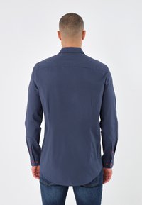 Camicia a maniche lunghe navy in cotone con colletto button-down, orlo curvo e bottoni rossi a contrasto sulle maniche.