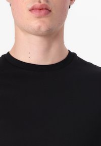 Fekete, rövid ujjú póló, amely kerek nyakkivágással rendelkezik. Az anyag simának tűnik, testhez simuló fazonnal, amely a nyak alatt bőrfelületet mutat.