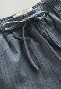 Grau melierte Shorts mit elastischem Bund und einer vorderen Kordel zum Binden. In der Nähe des Bundes befindet sich ein Etikett mit der Aufschrift "CONTAINS".