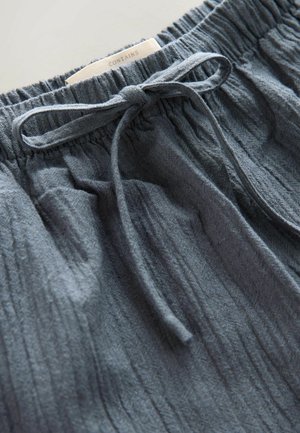 Grijze korte broek met een textuur en een elastische tailleband, voorzien van een strik aan de voorkant. Heeft een label met de tekst "CONTAINS" dicht bij de tailleband.