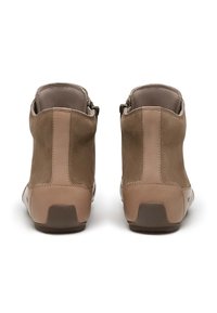 Un par de botas de ante beige hasta el tobillo visto desde atrás, con suelas de goma y cremalleras laterales, sobre un fondo blanco.
