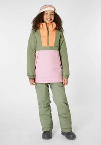 Felpa colorata con parte superiore arancione, maniche verdi e corpo rosa. Abbinata a pantaloni verdi e stivali neri. Tessuto texture, design funzionale.