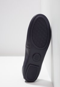 Czarna skórzana podeszwa z teksturowanej gumy, z okrągłym logo i żłobionymi akcentami. Czyste linie i subtelny detal szycia.