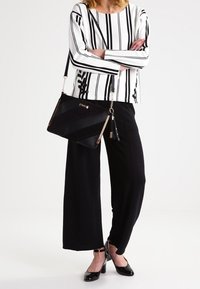 Svart och vit randig långärmad topp, vida svarta byxor, svart handväska med dragkedja och svarta skor. Texturerat tyg och linjär design.