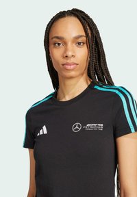 Sort atletisk skjorte med turkise og hvide accenter, prydet med et Mercedes-Benz logo og teksten "AMG PETRONAS Formel 1 Team". Korte ærmer.