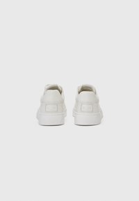 Adidași din piele albă cu o textură netedă, formă rotundă și tălpi din cauciuc. Prezintă un eticheta de branding discretă pe călcâi.