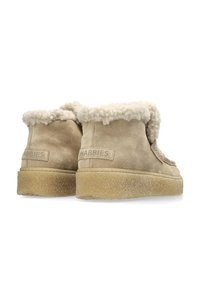 Beige suede boots with shearling trim, rounded shape, and textured rubber sole. Features stitched accents and branding on the side.