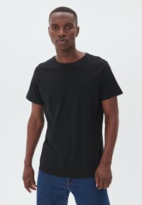 Sort crew neck t-shirt lavet af glat bomuld, med korte ærmer og løs pasform, parret med blå denim jeans.