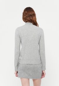 Siv turtleneck pulover iz mehke pletene tkanine, ki ima dolge rokave in ravno spodnji rob, v kombinaciji s usklajenim teksturiranim mini krilom.