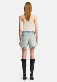Shorts in denim chiarissimo con orlo sfrangiato, abbinati a un top beige senza maniche e stivali in pelle nera al ginocchio. Cuciture chiare e design a cinque tasche.