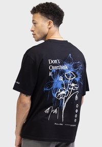 Black cotton t-shirt featuring a blue and white floral graphic on the back with the text "Don't Overthink it" above. Standard fit.
