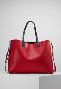 Duża czerwona skórzana torba na ramię o gładkiej teksturze i granatowych uchwytach. Posiada minimalistyczny design oraz odpinany pasek.