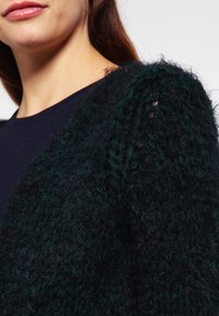 Tjock, strukturerad svart och mörkgrön stickad cardigan med en lös passform och unika puffade axeldetaljer som förbättrar den övergripande formen och designen.