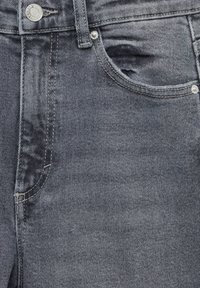 Gros plan sur un jean en denim noir montrant un bouton, une boucle de ceinture, une poche avant et des rivets avec des détails de couture visibles.
