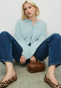 Lichtblauwe gebreide cardigan met een ronde hals, bruine handtas, oversized blauwe denim jeans en instappers met luipaardprint.