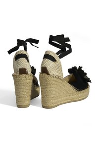 Schwarze Keil-Espadrilles mit gewobenem Jutefersen, ausgestattet mit einem schwarzen Band zum Binden und einer floralen Akzentuierung an der Vorderseite. Weicher Stoff-Oberteil, geschlossenes Heck.