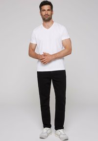 Weißes Baumwoll-V-Ausschnitt-T-Shirt kombiniert mit schwarzen Hosen und weißen Sportschuhen. Das Outfit ist einfach, ohne sichtbare Muster oder Akzente.