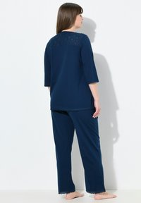 Námořnická modrá pyžamová souprava s topem se třičtvrtinovými rukávy, který má ozdobné krajkové detaily na zadní straně a krajkový lem na spodním okraji kalhot. Měkká tkanina.