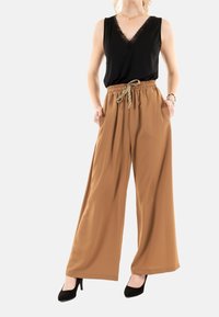 Top nero senza maniche con pizzo, abbinato a pantaloni larghi beige con cintura elasticizzata e lacci. Calzature: tacchi neri.