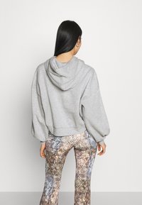 Felpa grigia corta con cappuccio, spalle abbassate e orlo a coste. Abbinata a leggings a stampa serpente multicolore e testurizzata.