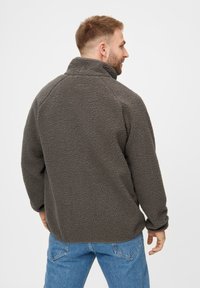 Pullover grigio in pile con colletto alto, superficie texturizzata e maniche raglan, dotato di orlo arrotondato e senza hardware visibile.
