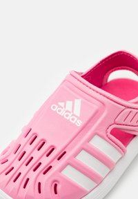 Chancla Adidas rosa con tres franjas blancas y orificios de ventilación, con una correa trasera y suela texturizada.