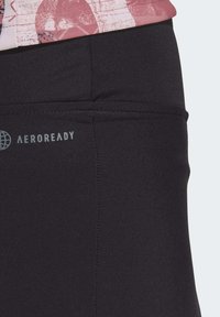 Juodos sportinės leggins su AEROREADY logotipu, pasižyminčios lygiu paviršiumi ir aukštu juosmeniu. Artimas juosmens ir audinio detalių planas.
