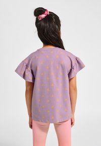 Fioletowa bawełniana koszulka z żółtym nadrukiem motyla, krótkie falbaniaste rękawy i okrągły dekolt, noszona z różowymi legginsami.