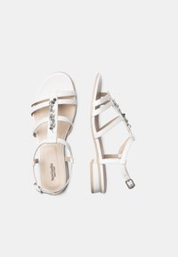 Sandali bianchi con diverse cinghie regolabili e un tacco sottile. Il design include dettagli metallici decorativi lungo le cinghie.