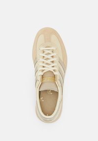 Cremfarbene Sneaker mit Obermaterial aus Wildleder und Textil, drei graue Streifen und goldenes Logo-Detail auf der Zunge. Flache Schnürsenkel und texturierte Innensohle.