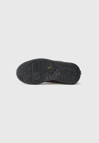 Sorte gummisåle til sneakers med teksturerte mønstre, inkludert sirkulære og trekantede former, samt en logo nær hælen.