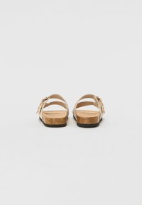 Sandales beiges avec plusieurs straps réglables, une semelle en liège et une semelle en caoutchouc texturé. Présente un accent décoratif près de la boucle.
