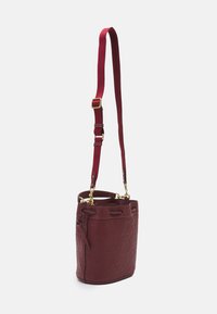 Borsa a secchiello in pelle bordeaux con motivo embossé, hardware dorato e tracolla regolabile a righe. Base rotonda, design aperto.
