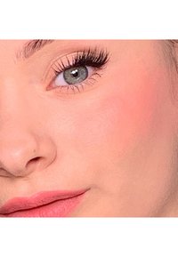 Gros plan sur un visage avec une peau claire, des yeux verts aux cils foncés et des lèvres roses douces, mettant en valeur une texture lisse et un blush naturel.