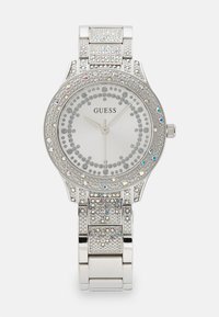 Montre en argent avec un cadran orné de pierres précieuses et un bracelet. Elle possède un cadran blanc avec des accents argentés, des embellissements en cristal et une forme ronde.