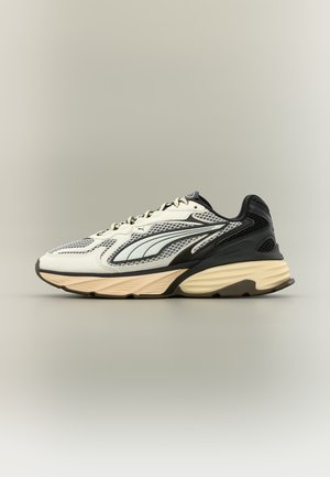 Chaussure de running à profil bas avec tige en mesh crème, noir et gris, semelle épaisse beige et design de bande latérale courbée, vue de profil.