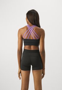 Svart sports-bh med kontrasterende lilla kryssremmer på baksiden og matchende svarte shorts, med en tettsittende design og glatt tekstur.