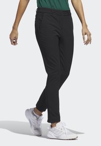 Svarta, figurnära byxor i mjukt, stretchigt tyg. Har en midja med medelhög höjd, framfickor och sidostygn. Kombineras med vita sportskor.