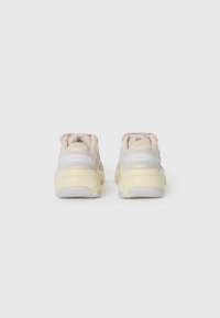 Beżowe i białe sneakersy w stylu retro z teksturowanym wykończeniem, wyściełanym kołnierzem i żółtą podeszwą. Posiadają stonowane logo na pięcie.