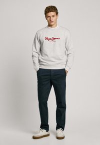 Gray sweatshirt features a red "Pepe Jeans London" logo, paired with dark navy pants and white sneakers with brown accents.