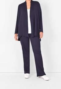 Marinblå stickad kofta med öppen framsida, långa ärmar, matchad med ribbade byxor. Vit V-ringad topp under och vita sneakers.